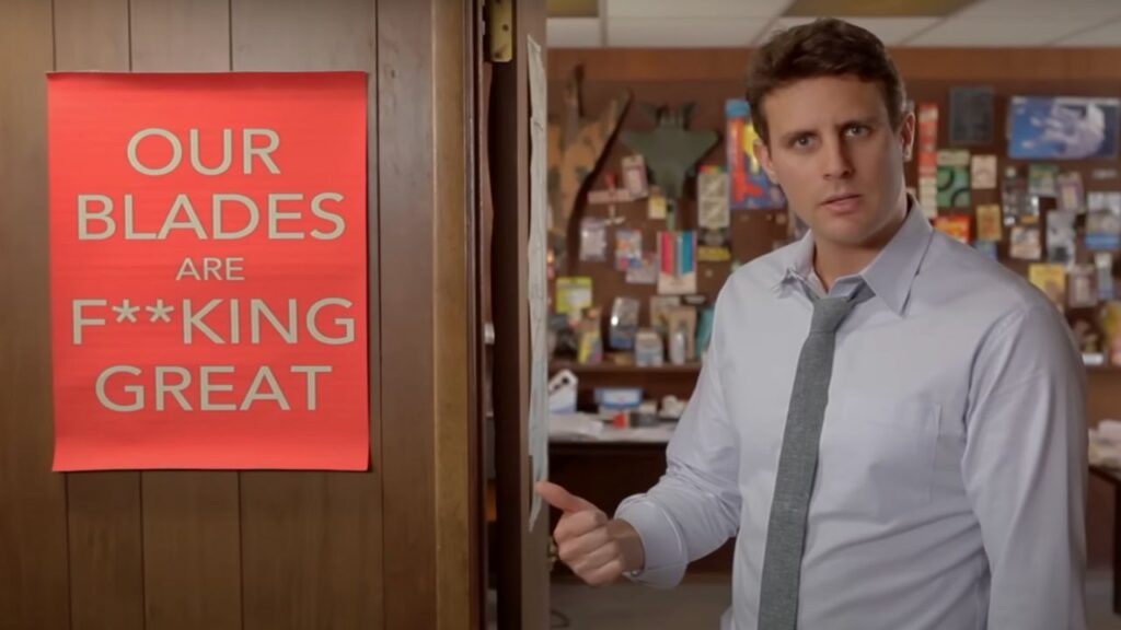 Una scena del video di Dollar Shave Club, in cui il CEO indica un cartello rosso con su scritto "Le nostre lamette sono fo**utamente fantastiche"